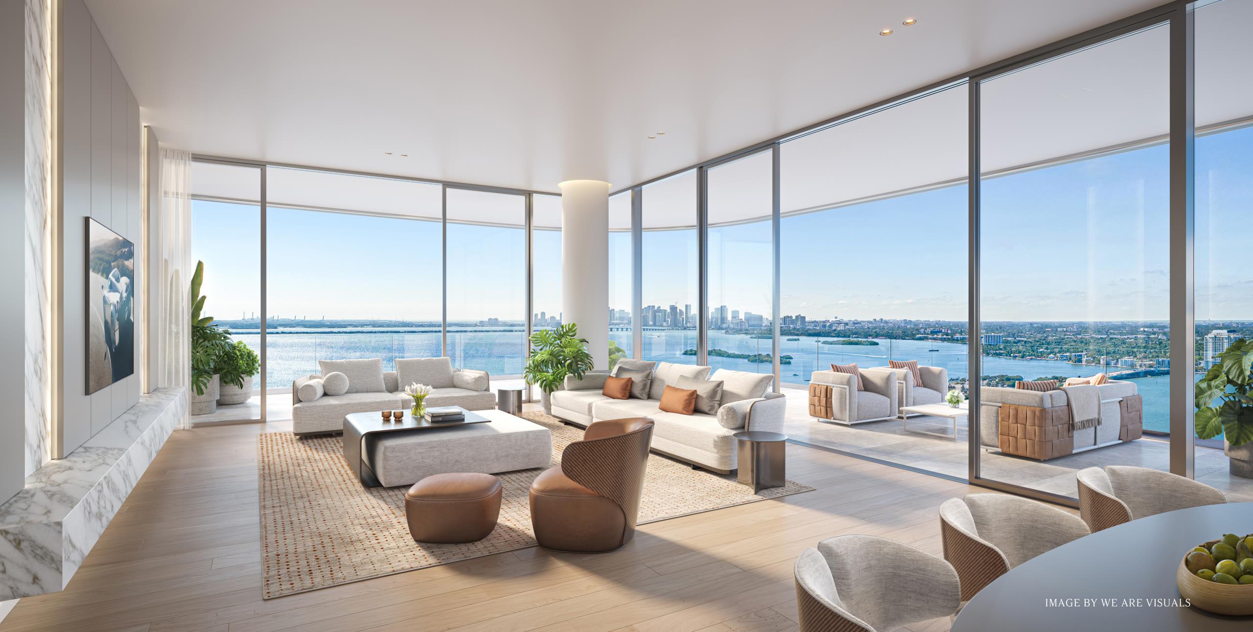 A corner living room with travertine surfaces and floor-to-ceiling glass opening onto a terrace above Biscayne Bay